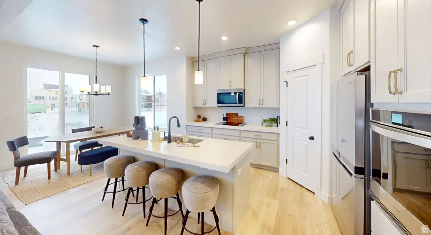 Kitchen with stainless steel appliances, light wood finished floors, recessed lighting, pendant lighting, and a chandelier
