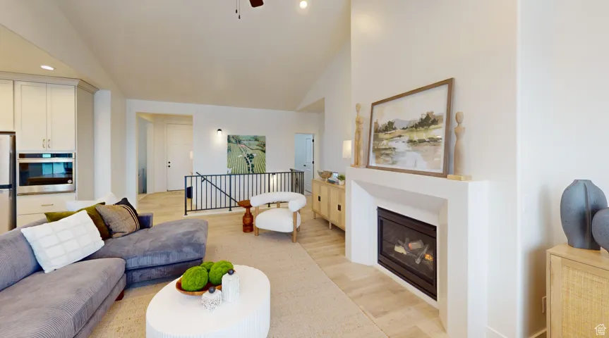 Living area featuring light wood finished floors, a glass covered fireplace, recessed lighting, a ceiling fan, and high vaulted ceiling