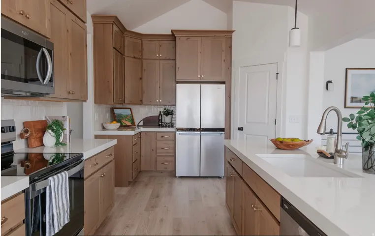 Kitchen featuring stainless steel appliances, pendant lighting, light wood-type flooring, backsplash, and vaulted ceiling
