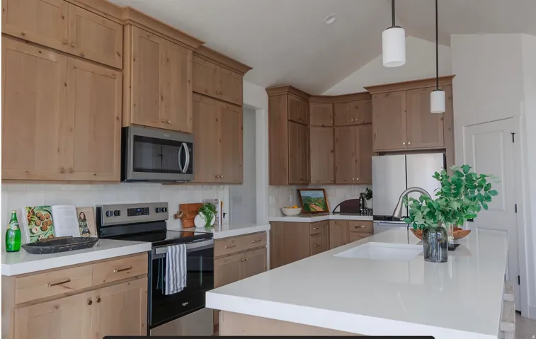 Kitchen featuring appliances with stainless steel finishes, a center island with sink, backsplash, lofted ceiling, and hanging light fixtures