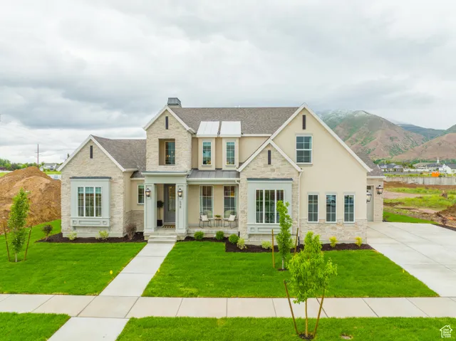 View of front of house with stone siding, a front yard, a standing seam roof, covered porch, and a shingled roof