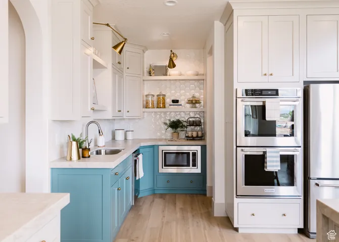 Kitchen featuring white cabinetry, open shelves, appliances with stainless steel finishes, blue cabinets, and tasteful backsplash