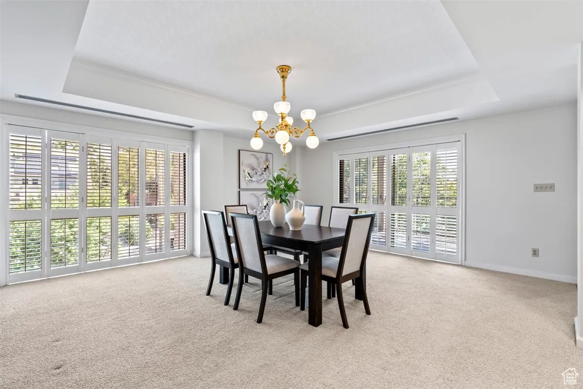 Dining area with a raised ceiling, light carpet, and a chandelier