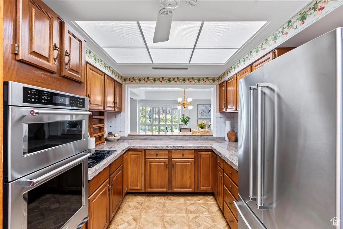 Kitchen with brown cabinets, stainless steel appliances, a chandelier, light countertops, and backsplash