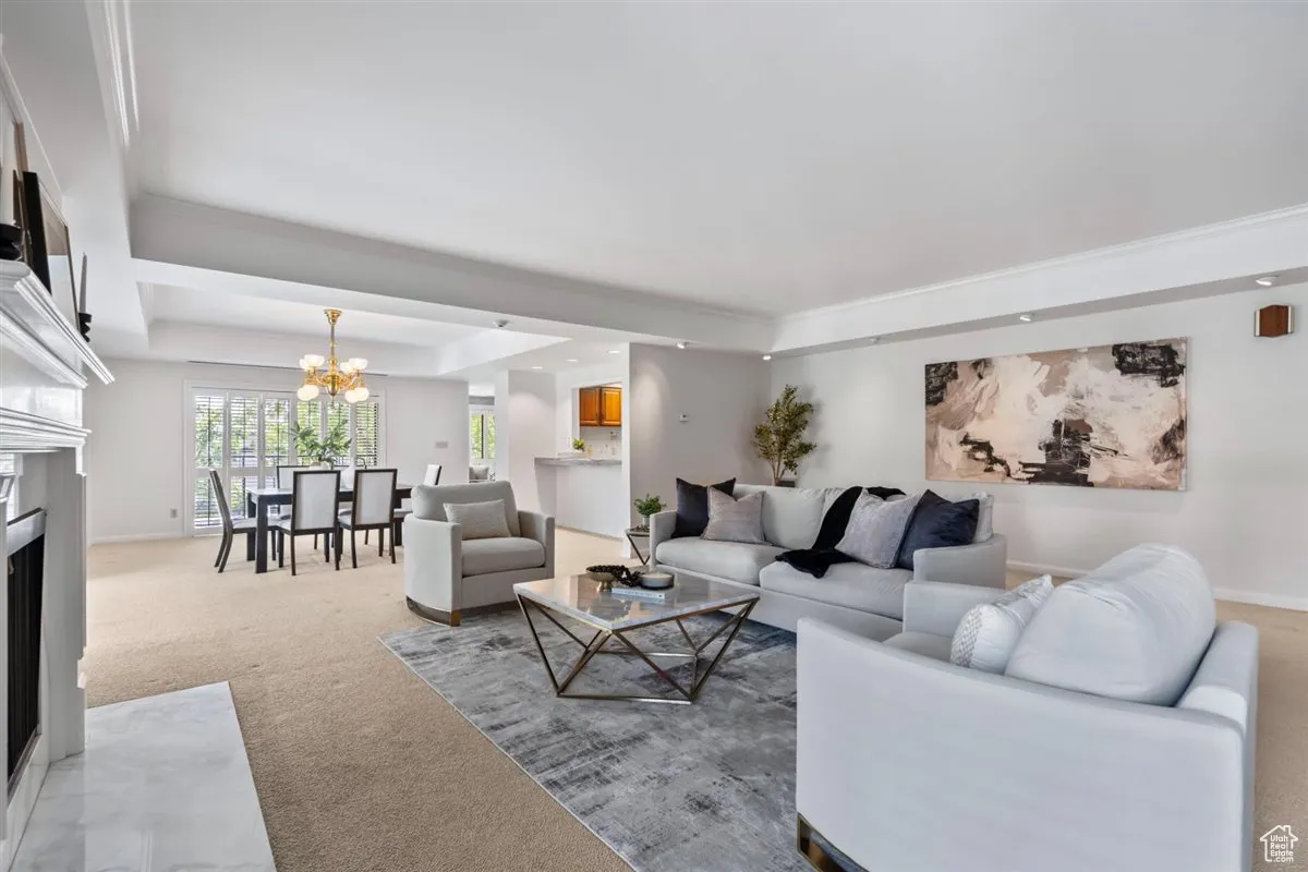 Living room with a fireplace with flush hearth, a tray ceiling, carpet flooring, a chandelier, and ornamental molding