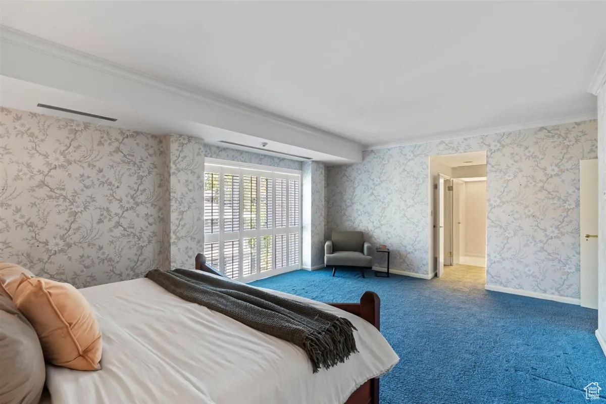 Bedroom featuring wallpapered walls, crown molding, and carpet flooring