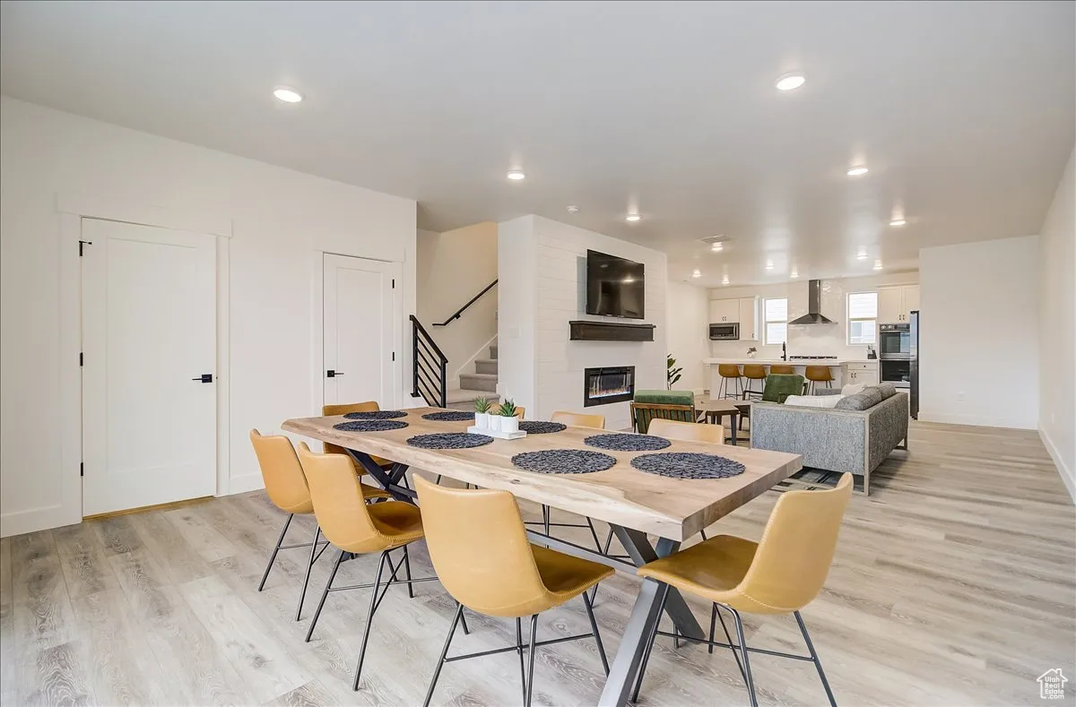 Dining room with a large fireplace, light wood-type flooring, stairway, and recessed lighting