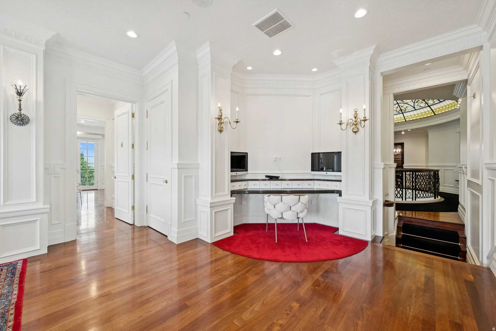 Hardwood flooring extending throughout, featuring intricate wall paneling and decorative sconces