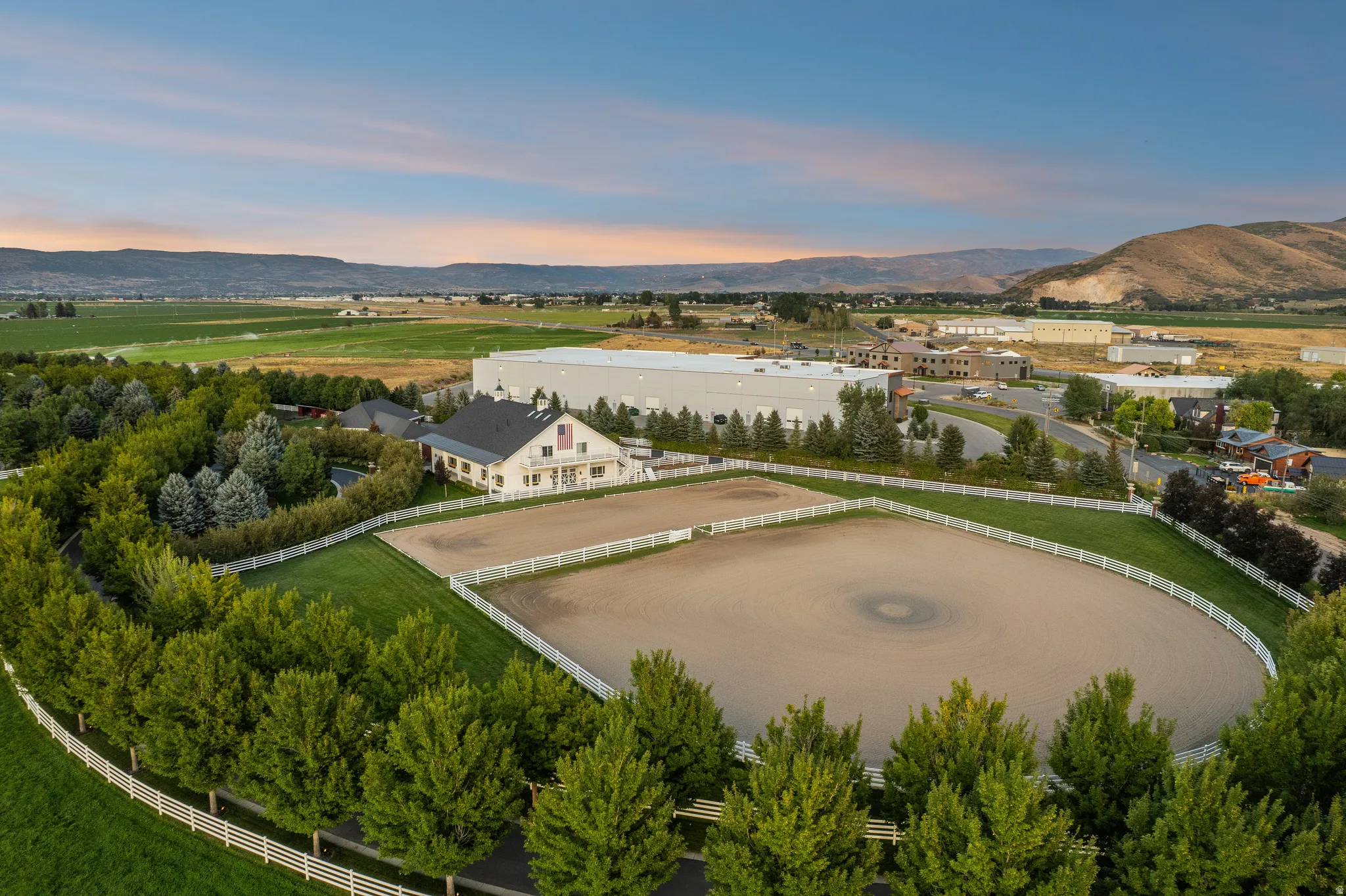 Expansive equestrian property featuring a large arena with white fencing, a manicured lawn, and mature trees