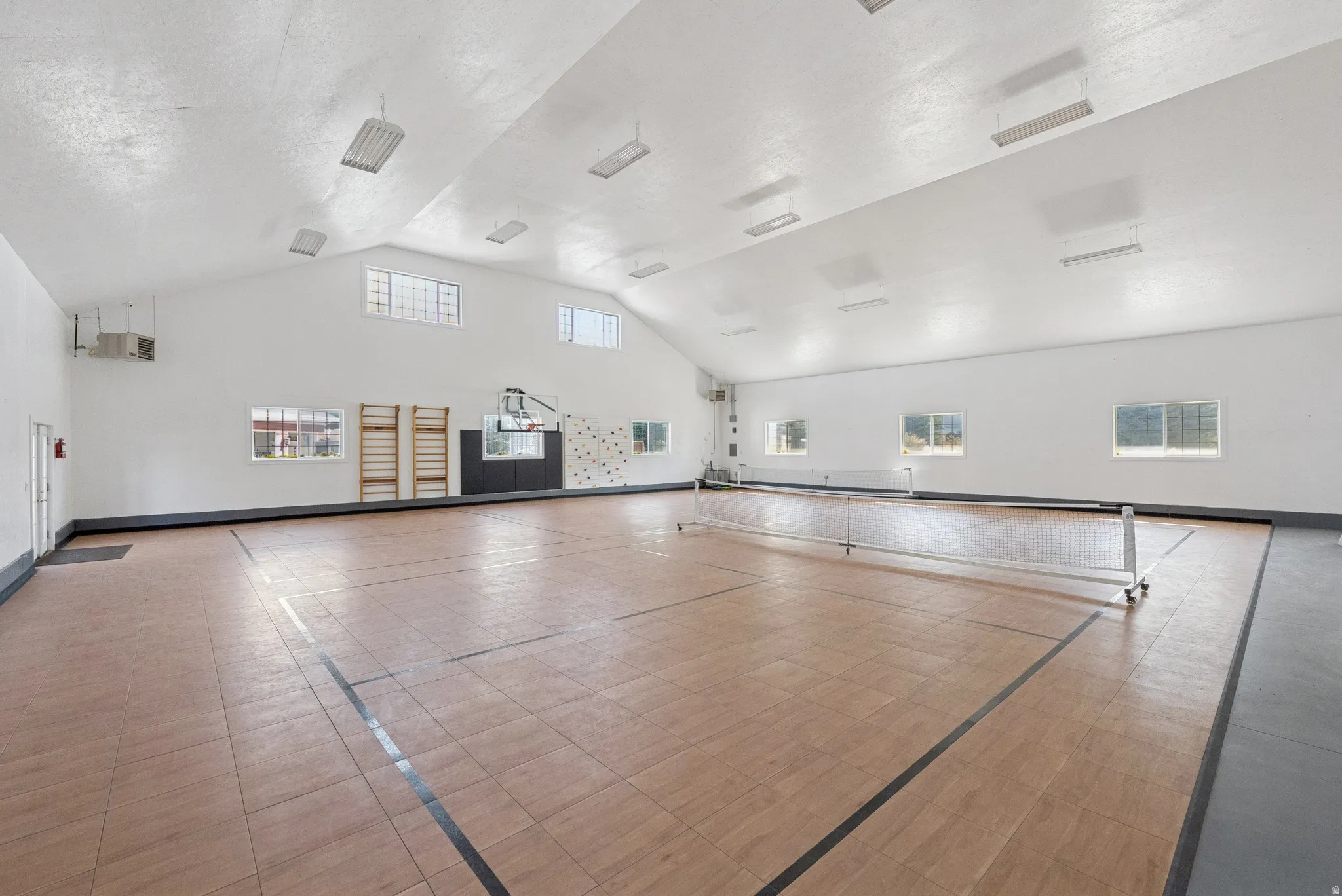 Spacious indoor court featuring wood-look flooring, multiple windows providing natural light, and a high vaulted ceiling