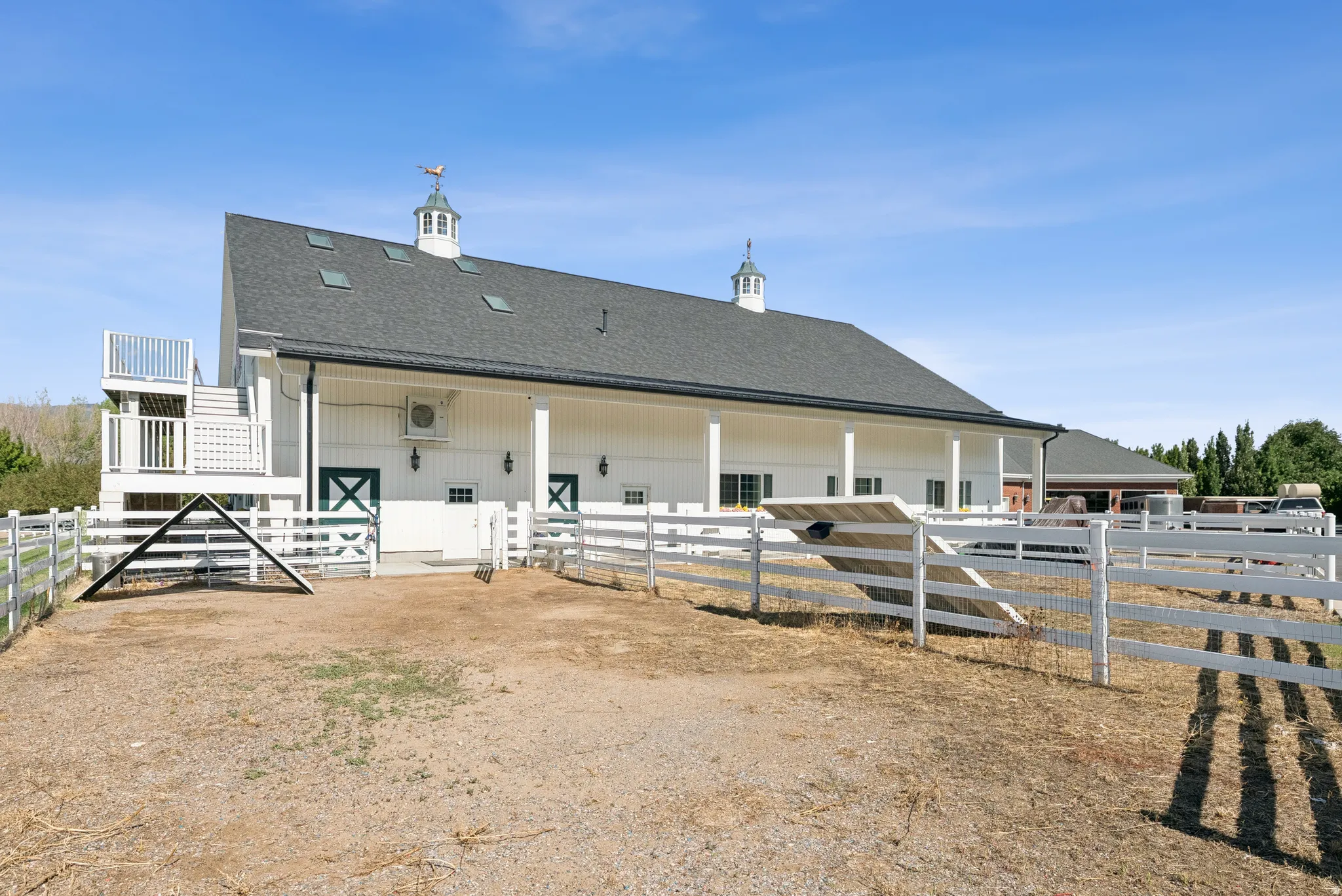 White barn-style structure featuring a dark gray shingle roof, multiple skylights, and a cupola with a weathervane