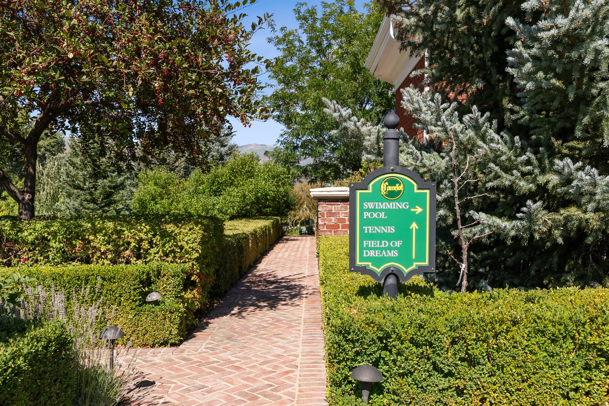 Brick paver pathway bordered by manicured hedges and mature trees