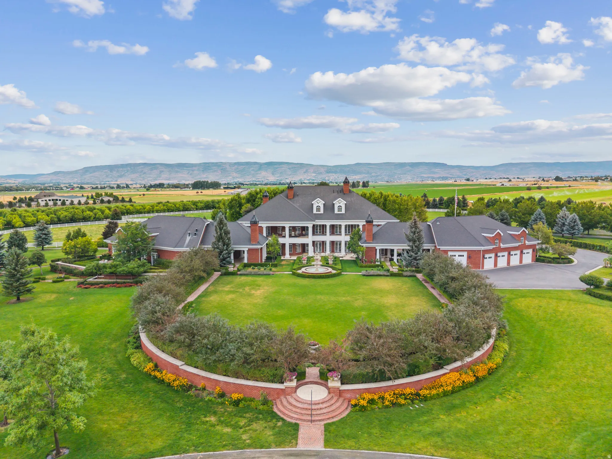 Expansive estate featuring a large main residence with brick exterior and multiple dormer windows, a grand circular driveway, and a separate multi-car garage building