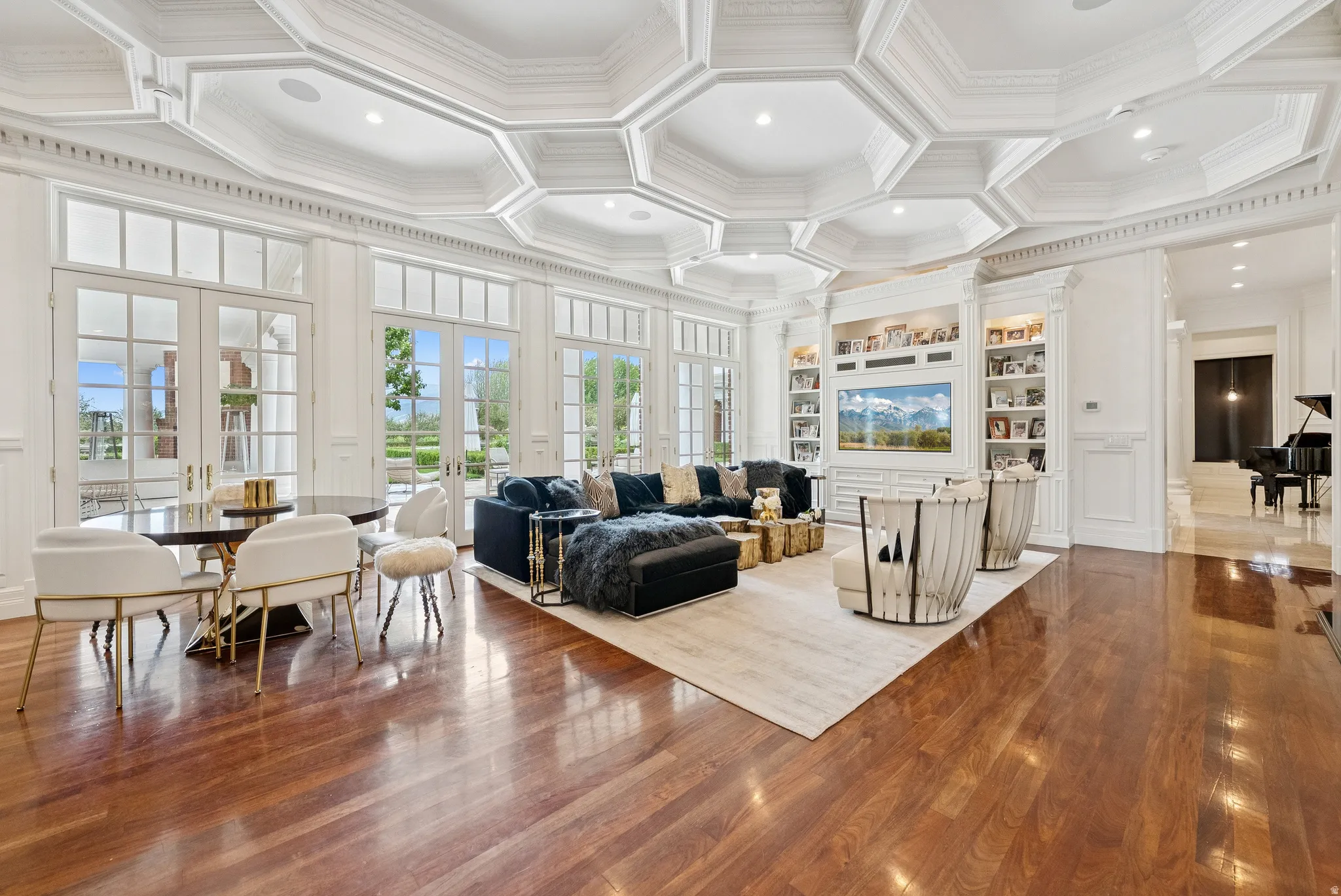 Expansive room featuring ornate coffered ceilings, rich wood-finish flooring, and multiple sets of French doors with transom windows
