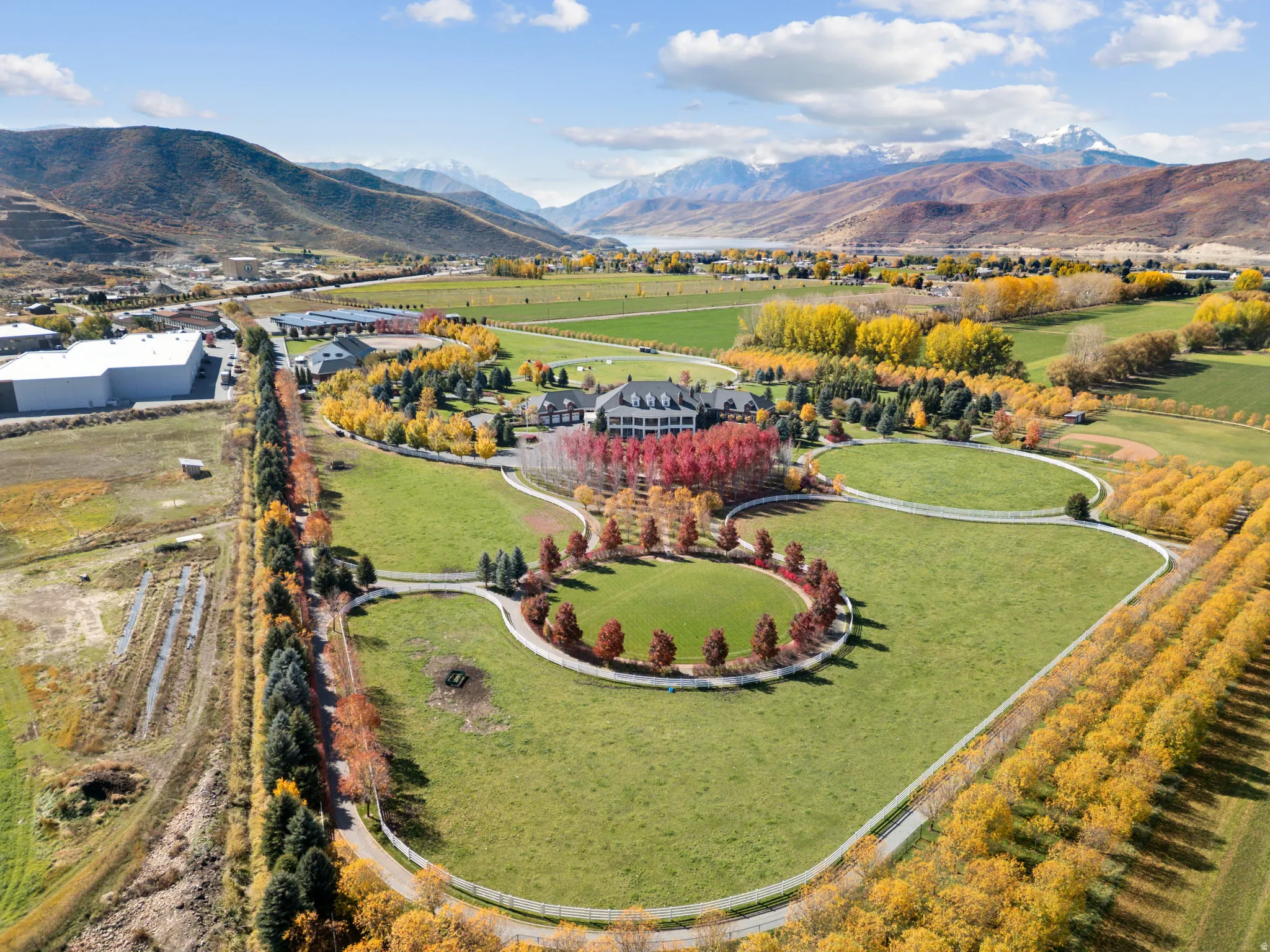 Extensive property featuring a large estate house, multiple outbuildings, vast green lawns, mature trees, and a mountain backdrop