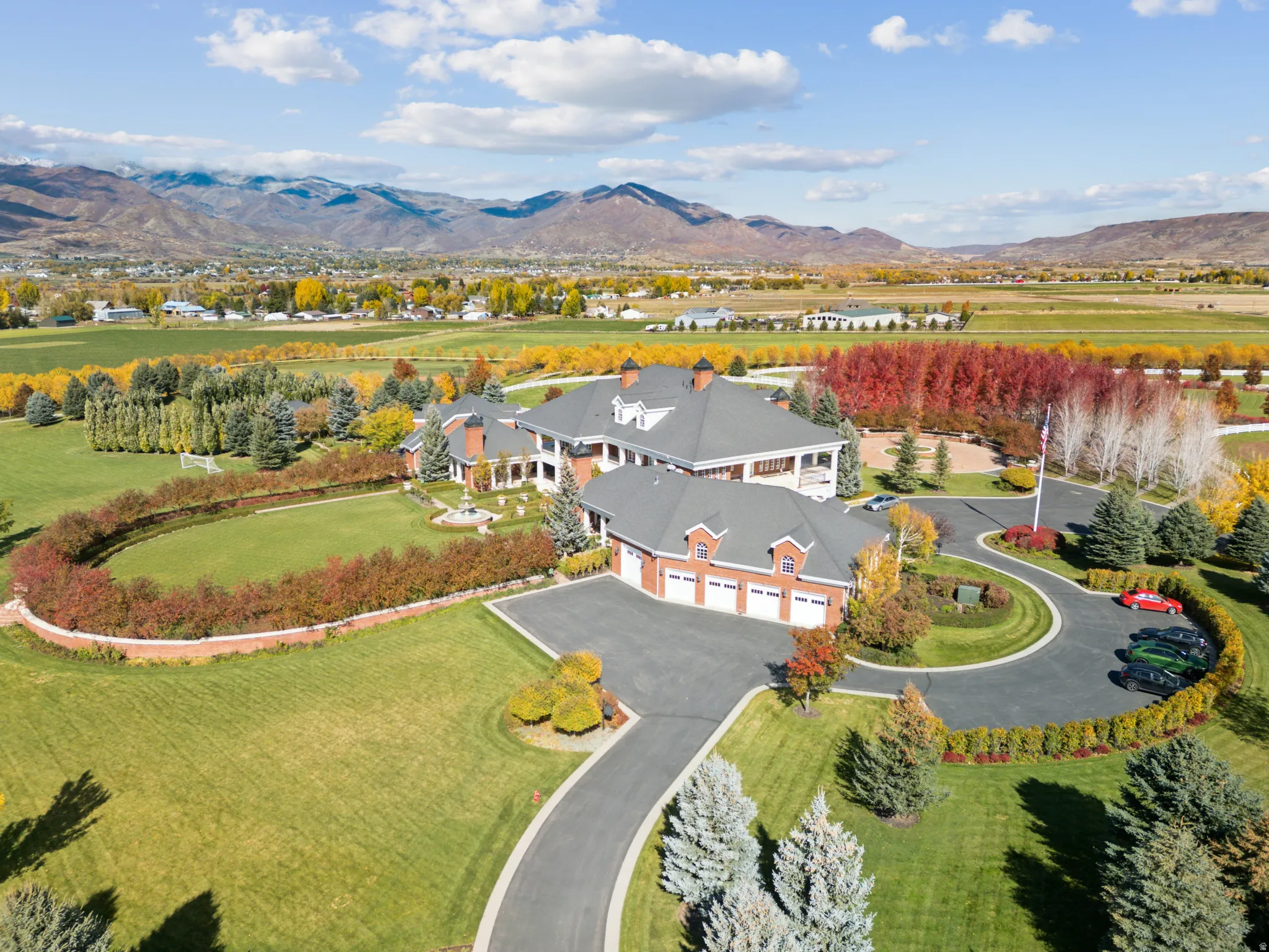 Expansive property featuring a multi-structure residence with red brick and white siding accents, a circular driveway, and a three-car garage