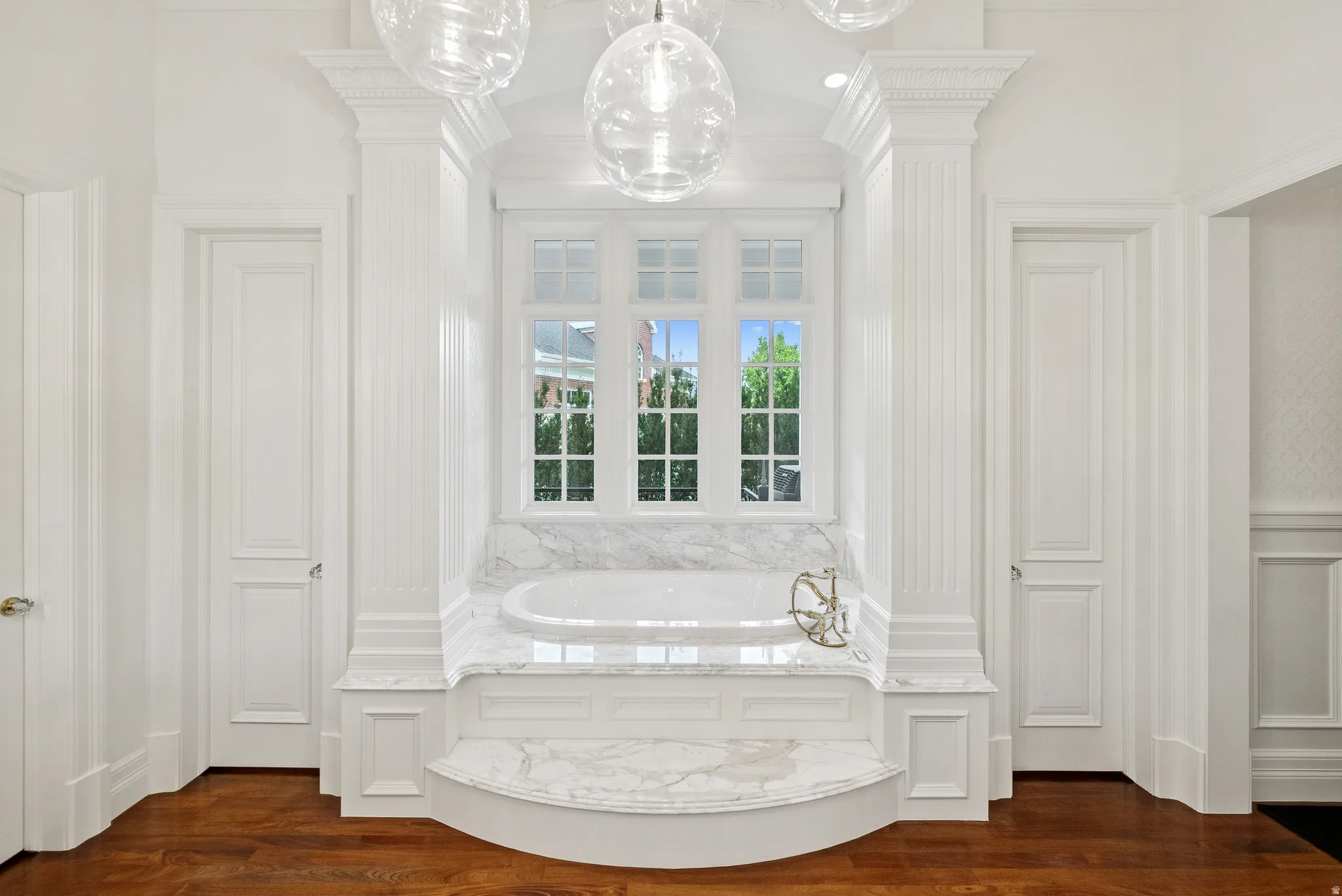 Soaking tub set within a marble surround, flanked by fluted columns and paneled walls