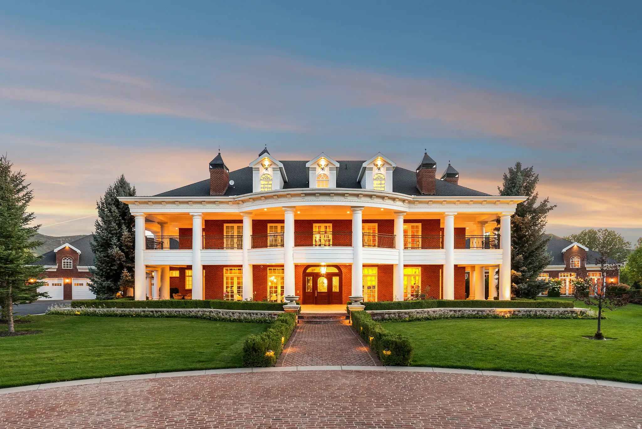 Stately brick residence featuring a two-story portico with white columns, multiple dormer windows, and a classic black shingle roof