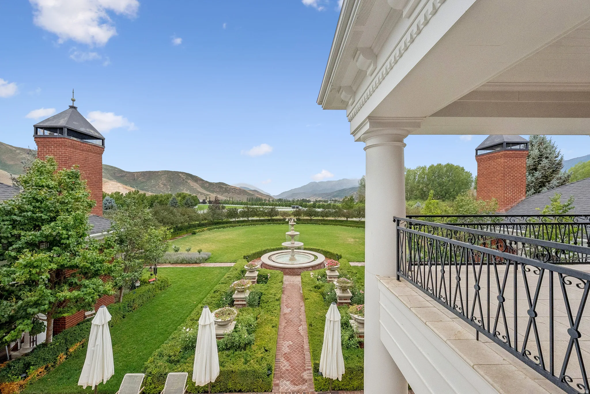 Expansive formal garden featuring a tiered fountain, intricate brick pathways, and manicured hedges