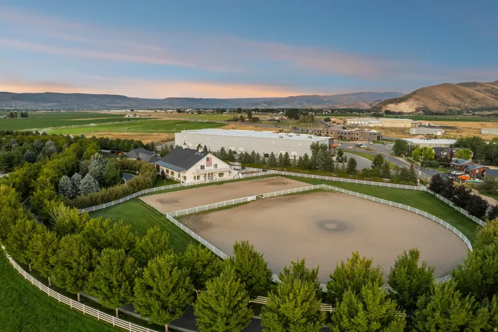 Expansive equestrian property featuring a large arena with white fencing, a manicured lawn, and mature trees