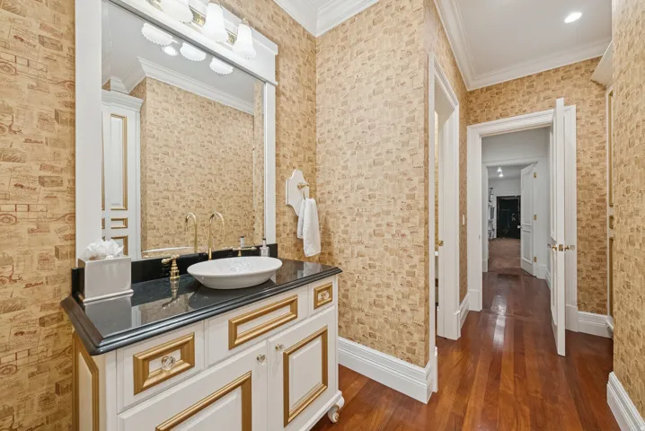 Vanity featuring a vessel sink, black countertop, gold-tone fixtures, and white cabinetry with gold trim