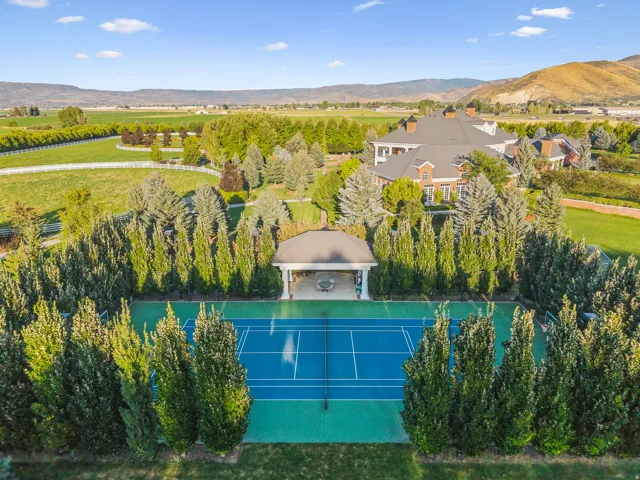 Full-size tennis court with a blue playing surface and green surrounds, bordered by mature evergreen trees