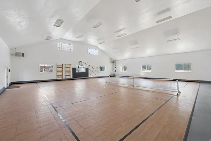 Spacious indoor court featuring wood-look flooring, multiple windows providing natural light, and a high vaulted ceiling