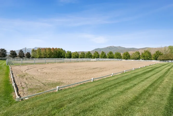 Expansive outdoor riding arena with a sand surface, bordered by white fencing