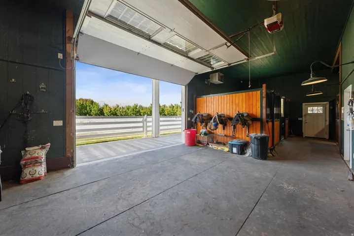 Spacious interior barn area featuring a large overhead door, concrete flooring, rich wood-paneled walls, and built-in lighting fixtures