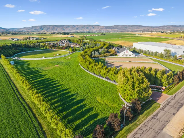 Expansive green acreage featuring a round riding arena, additional rectangular riding arena, and mature trees providing natural screening