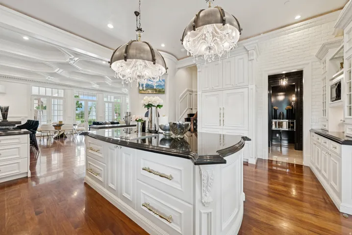 Gourmet kitchen featuring a large island with dark stone countertops, custom white cabinetry, and two ornate chandeliers