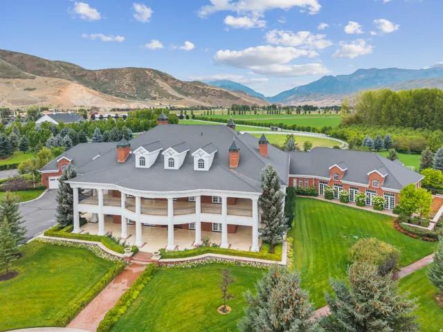 Expansive estate featuring a red brick exterior with white trim, a multi-level wrap-around porch, mature landscaping, a paved driveway, and mountain scenery