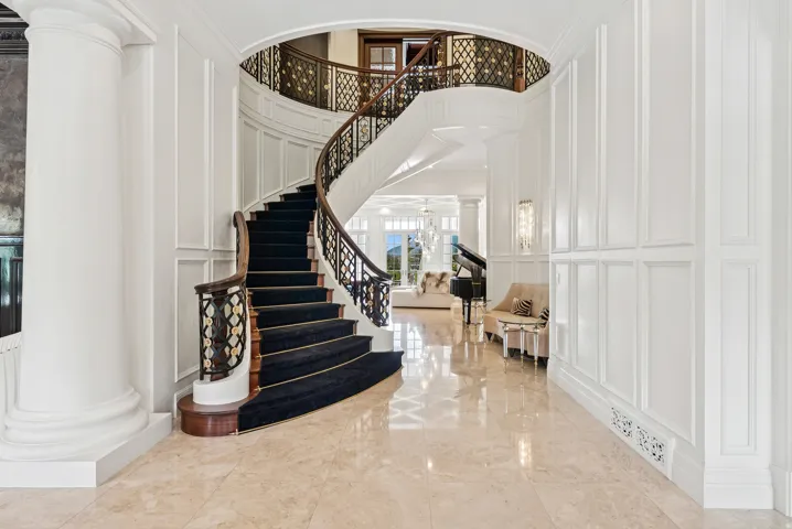 Grand entry featuring a curved staircase with dark wood handrails and ornate balusters, complemented by a black carpet runner