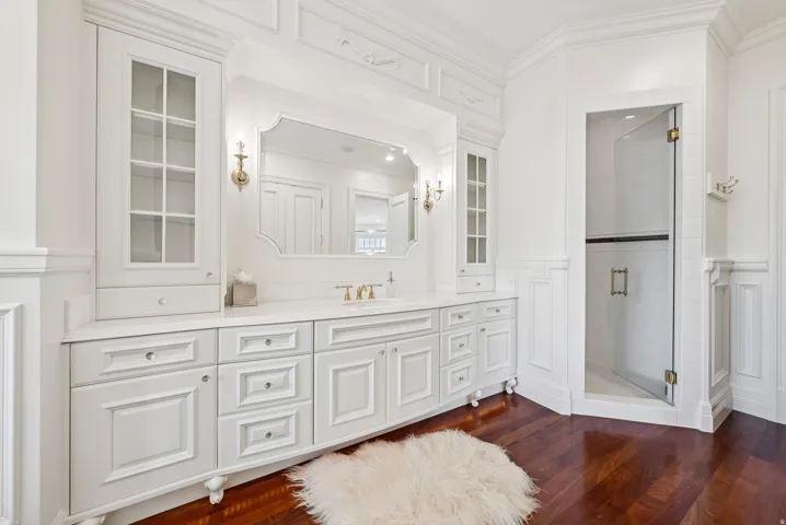 White custom cabinetry with glass-front display cabinets, a recessed vanity mirror, and dual wall sconces