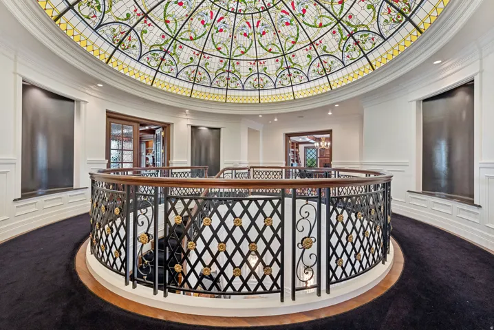 Grand foyer featuring a domed stained-glass ceiling, ornate wrought iron and wood-finish railing, dark carpeting, and built-in wall fountains