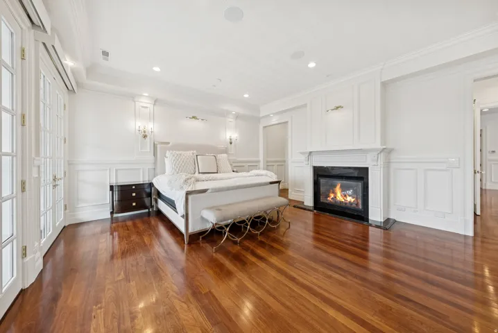 Spacious room featuring rich wood-finish flooring, white paneling, and a classic fireplace with a black surround
