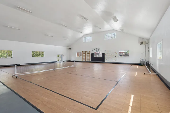 Spacious interior athletic court featuring wood-finish flooring with court lines, a full-height ceiling, multiple windows, and recessed lighting