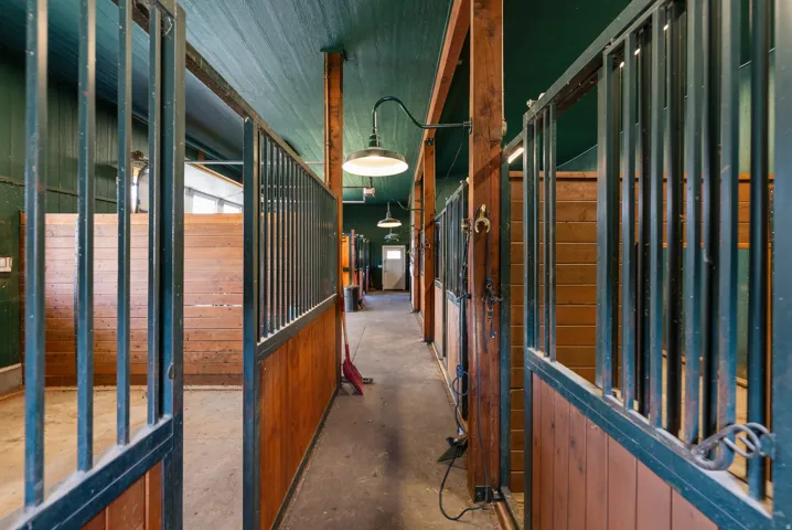Barn interior featuring multiple stalls with wood paneling and metal grates