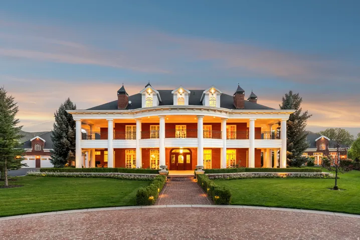 Stately brick residence featuring a two-story portico with white columns, multiple dormer windows, and a classic black shingle roof
