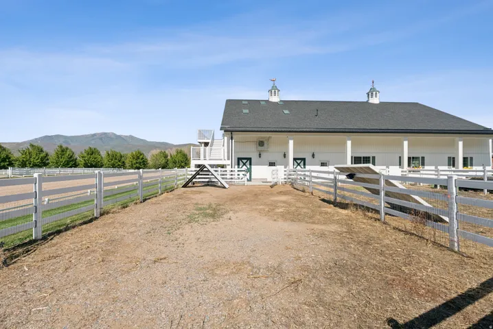 White barn structure featuring a dark shingle roof, two cupolas with weather vanes, and a surrounding white fence