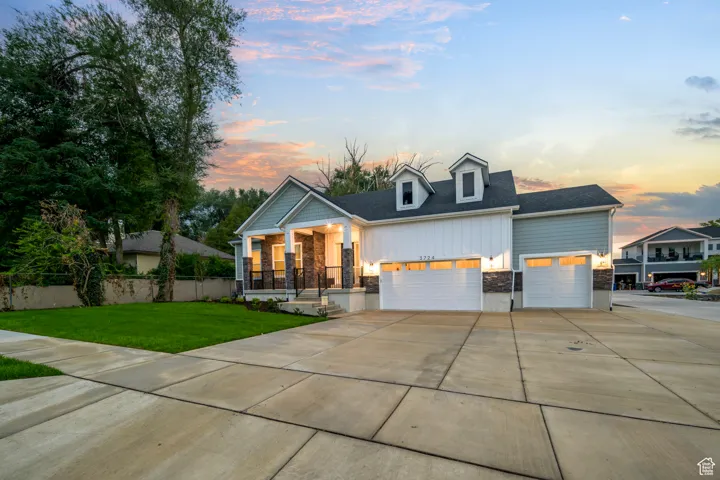 View of front facade featuring covered porch, driveway, stone siding, a lawn, and an attached garage
