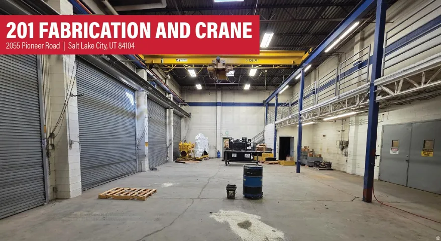 Spacious industrial interior featuring multiple roll-up doors, an overhead crane system, exposed ceiling joists, and concrete flooring