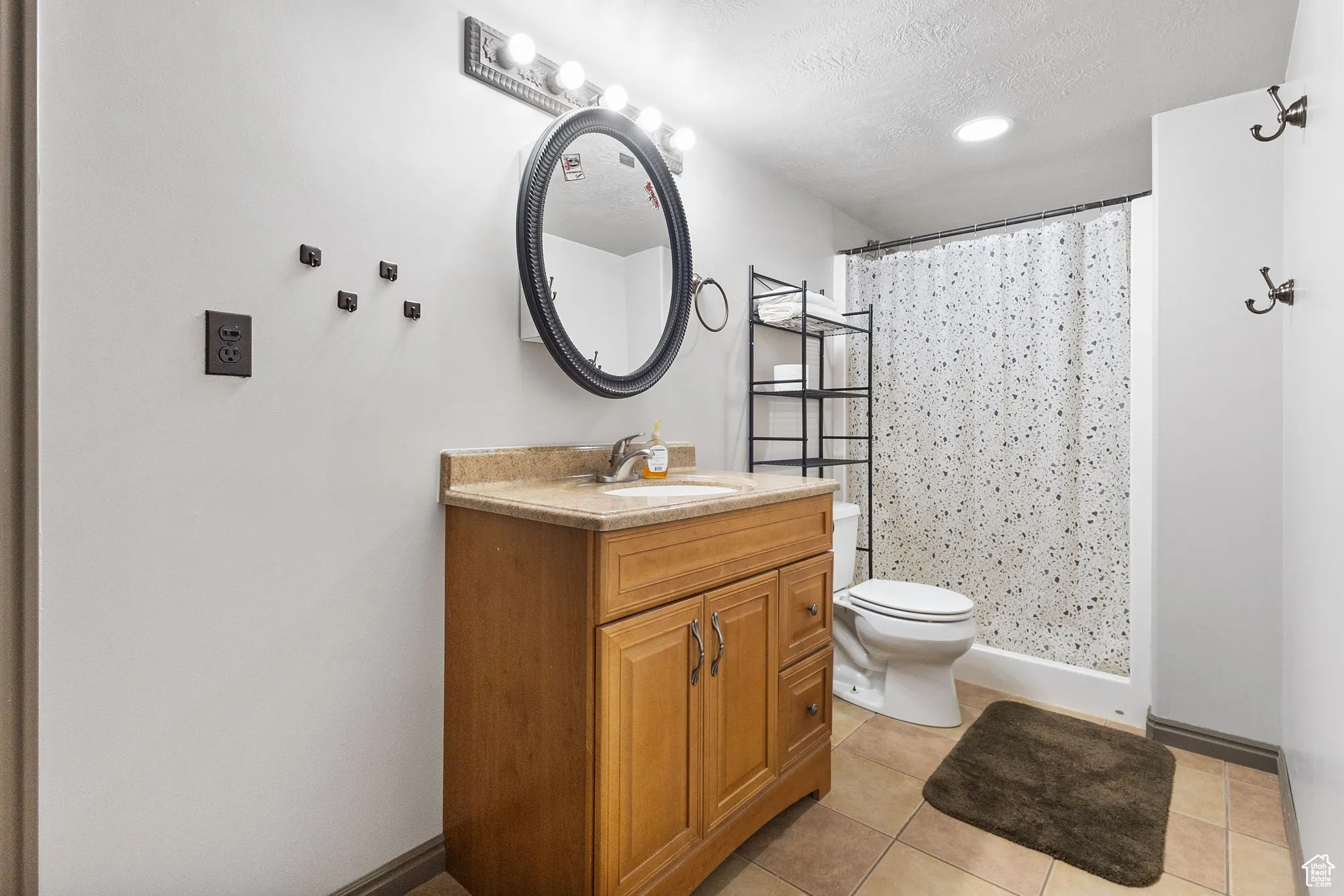 Bathroom featuring vanity, a textured ceiling, light tile patterned floors, and curtained shower