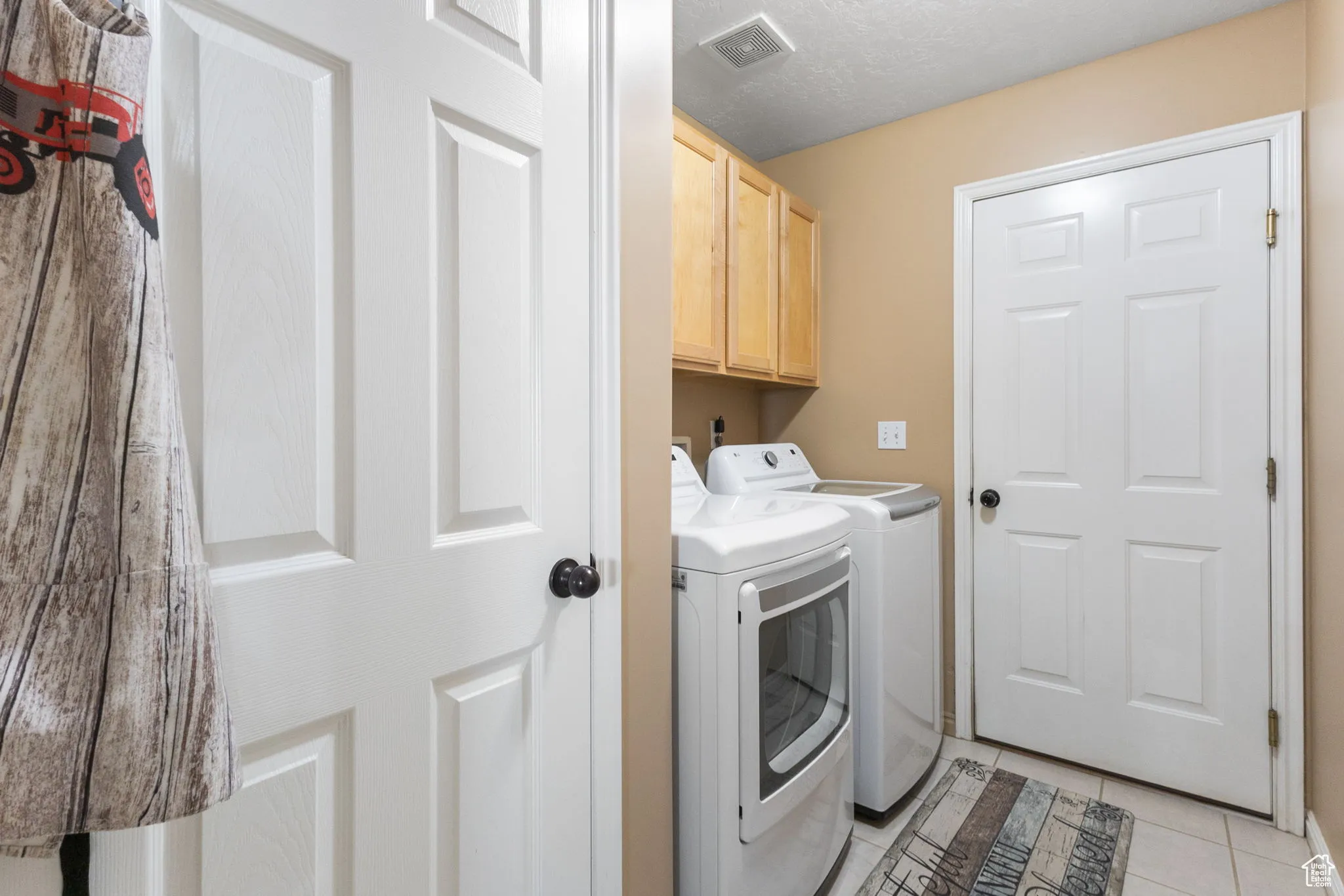 Laundry area featuring light tile patterned floors, washing machine and clothes dryer, cabinet space, and a textured ceiling