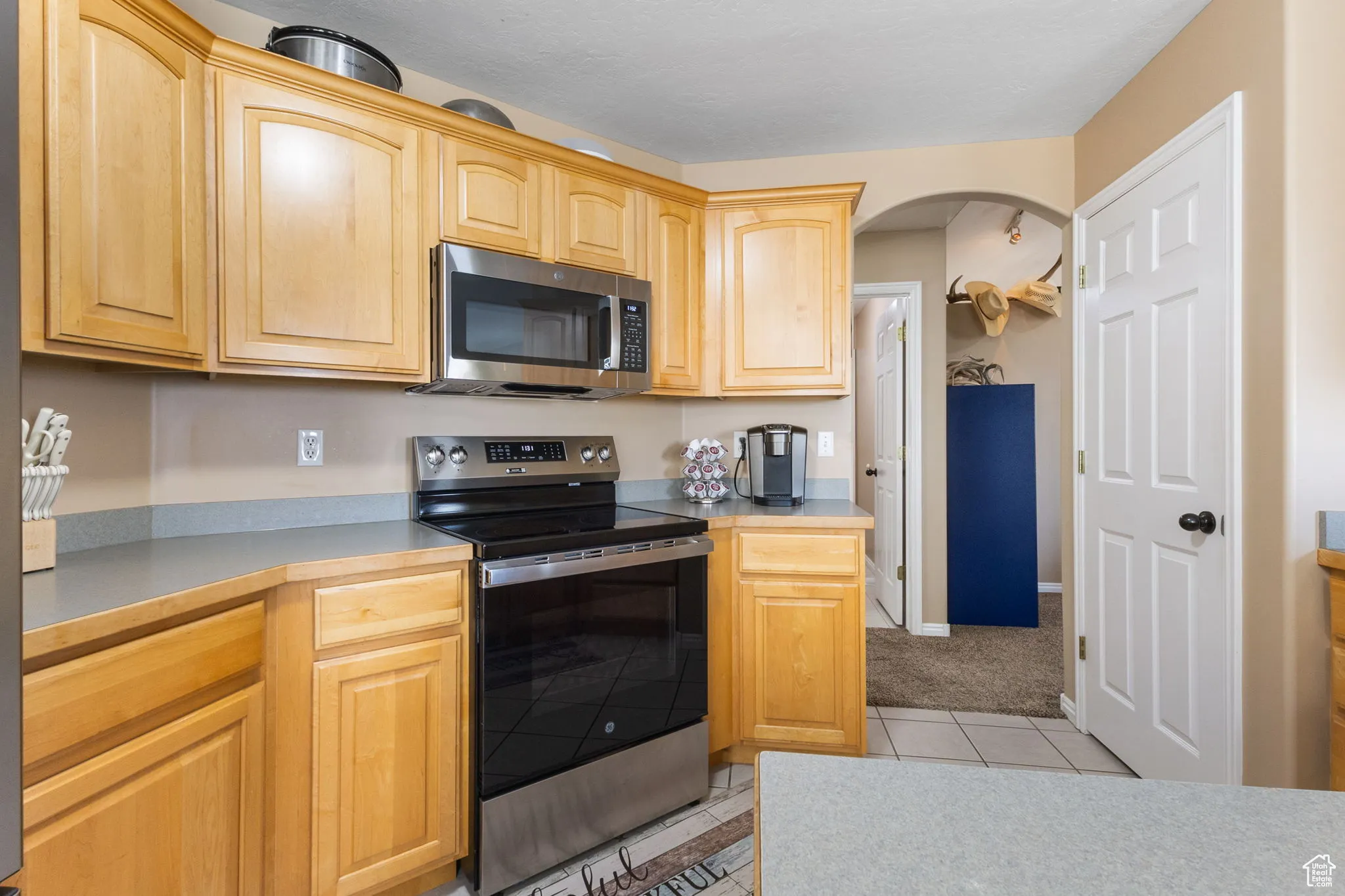 Kitchen featuring appliances with stainless steel finishes, light tile patterned floors, light countertops, light brown cabinets, and arched walkways