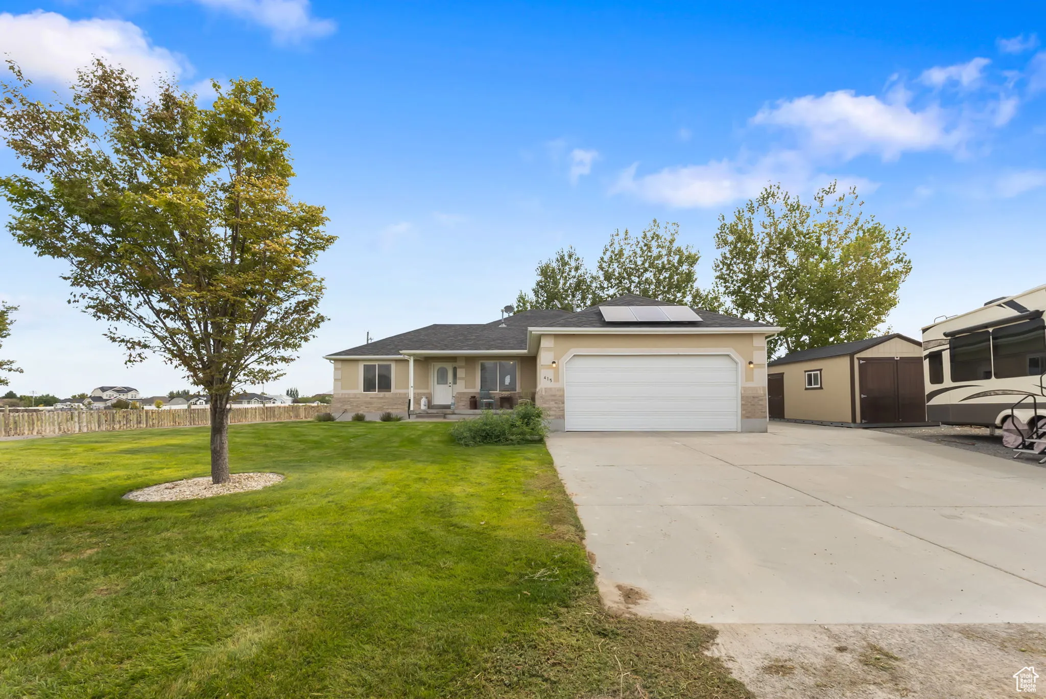 Single story home featuring roof mounted solar panels, driveway, a garage, an outdoor structure, and brick siding