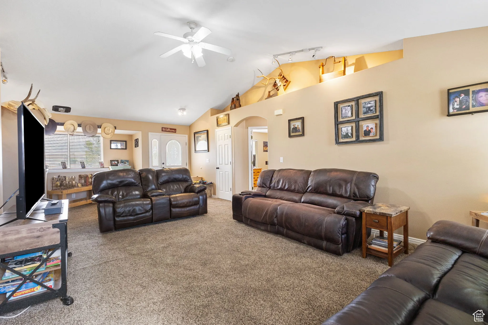 Carpeted living area with track lighting, arched walkways, lofted ceiling, and a ceiling fan