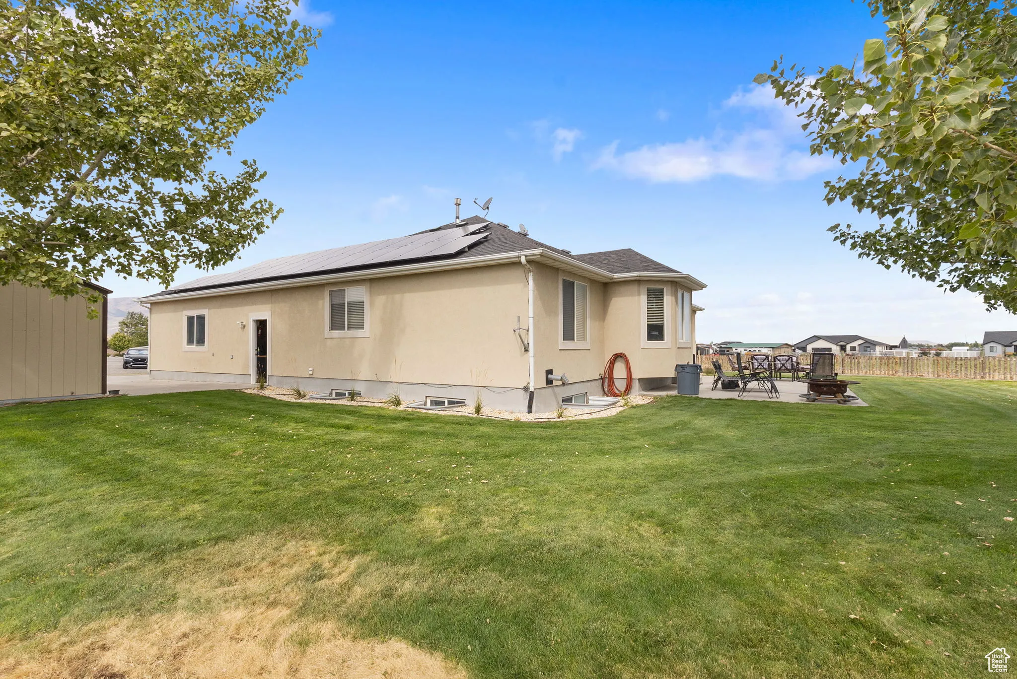 Rear view of house with a patio area, roof mounted solar panels, and a fire pit