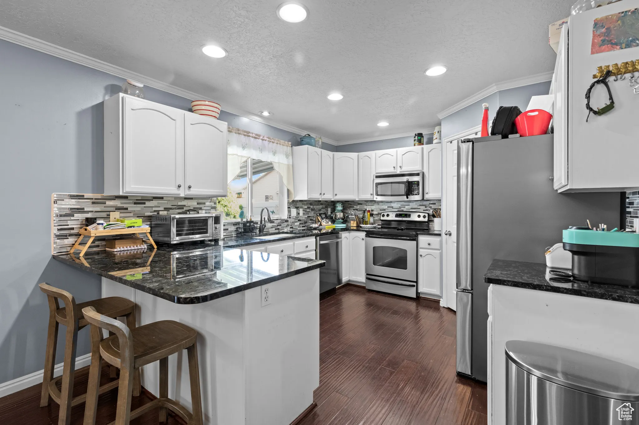 Kitchen with ornamental molding, a peninsula, a textured ceiling, white cabinets, and dark stone countertops