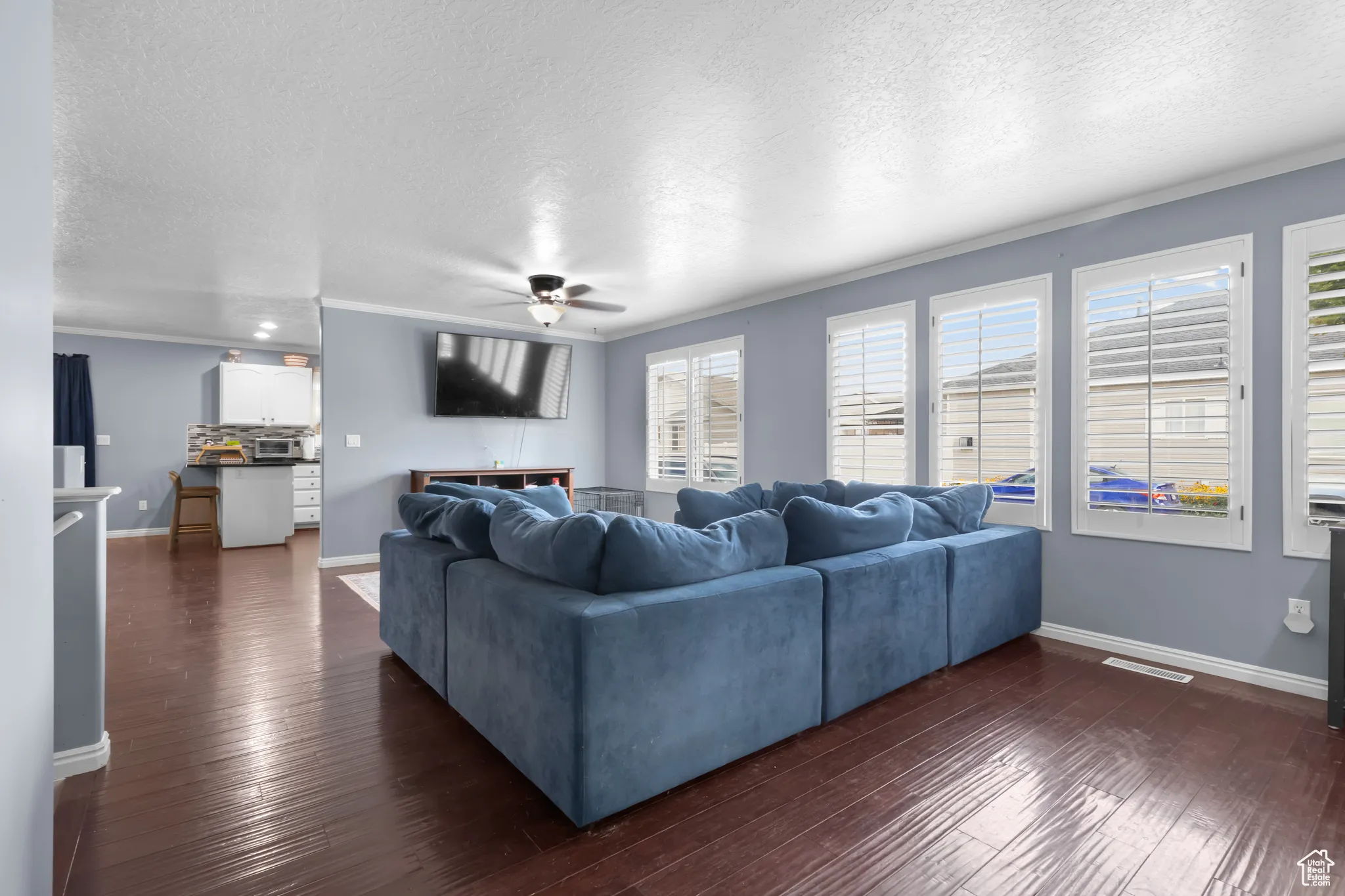 Living room with a textured ceiling, ornamental molding, dark wood finished floors, and a ceiling fan